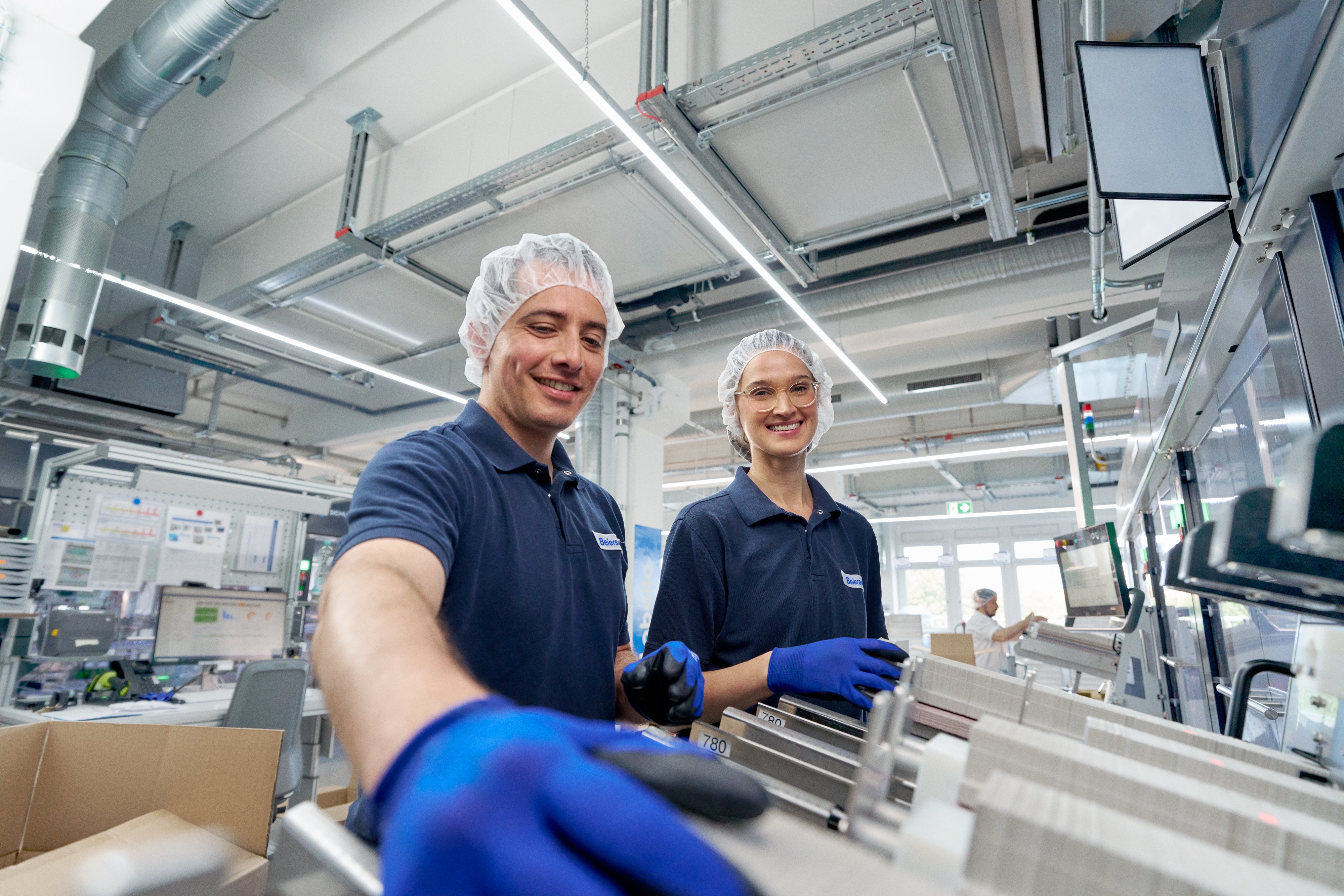 Two people in workwear operating a machine, one smiling at the camera.