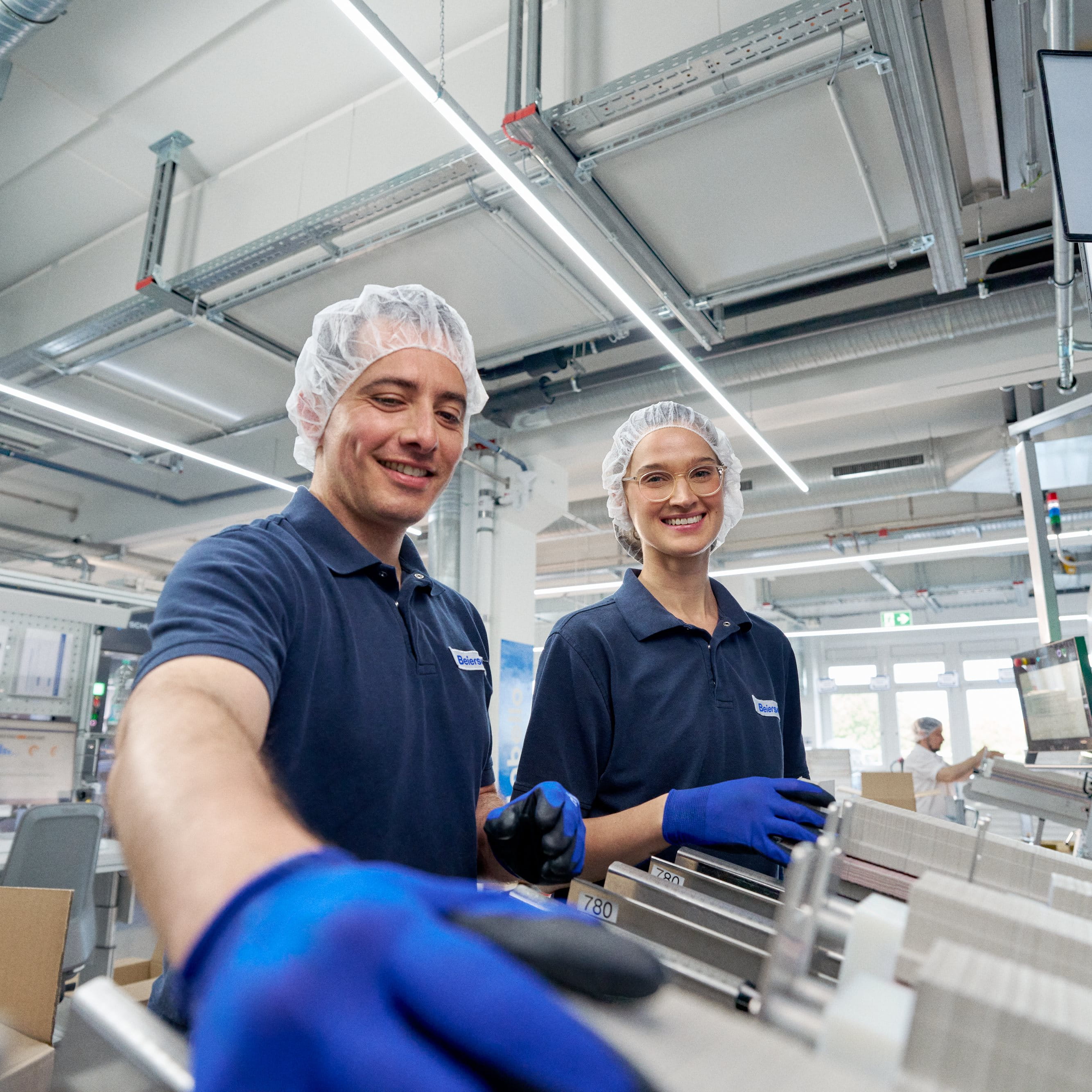 Two people in workwear operating a machine, one smiling at the camera.