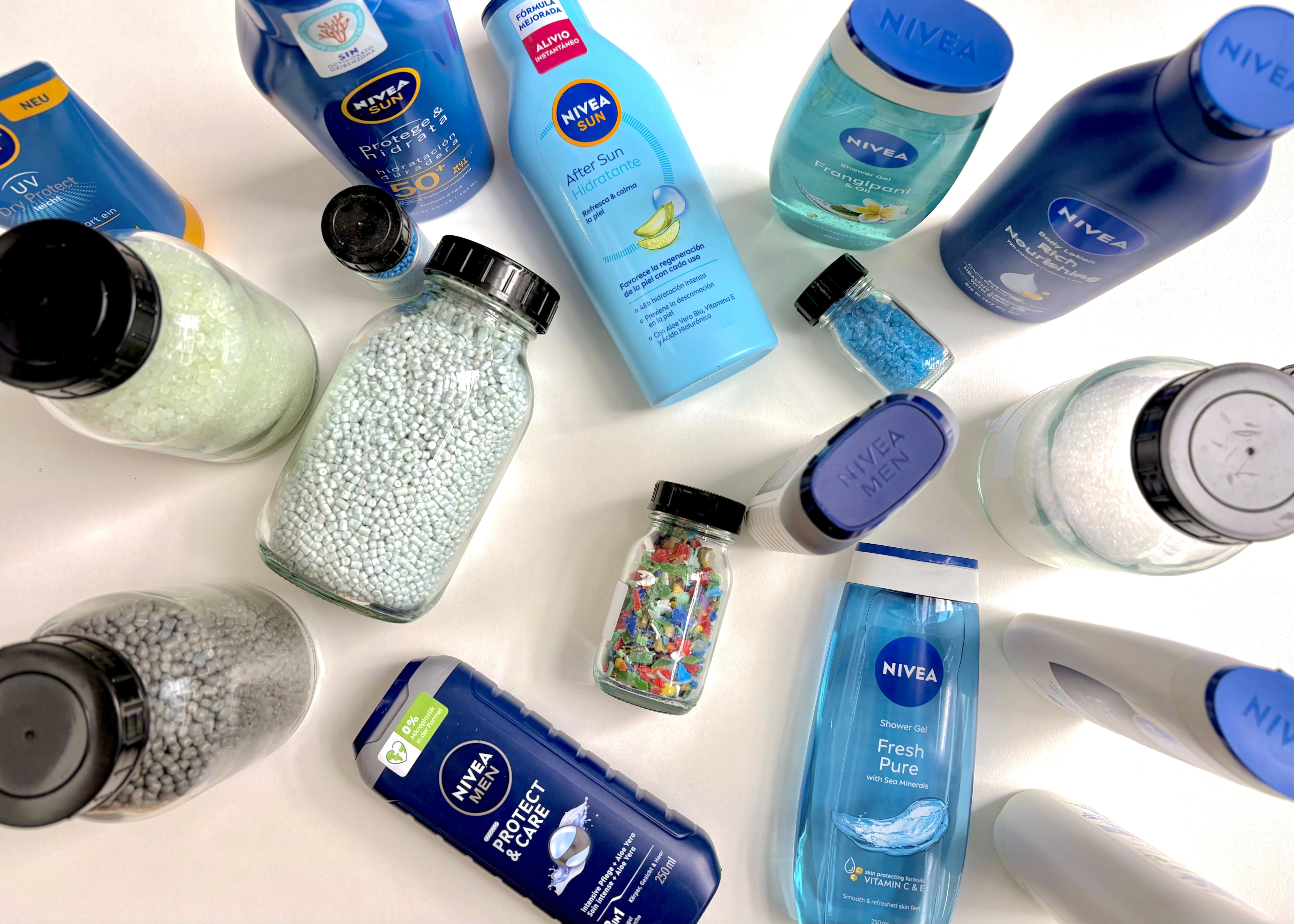 NIVEA Körperpflege- und Sonnenschutzprodukte sind kreisförmig um Tiegel angeordnet, die recycelte Kunststoffgranulate und Kunststoffflocken enthalten. Dies veranschaulicht nachhaltige Verpackungsinnovationen und die Verwendung von Recyclingmaterialien in Kunststoffverpackungen.