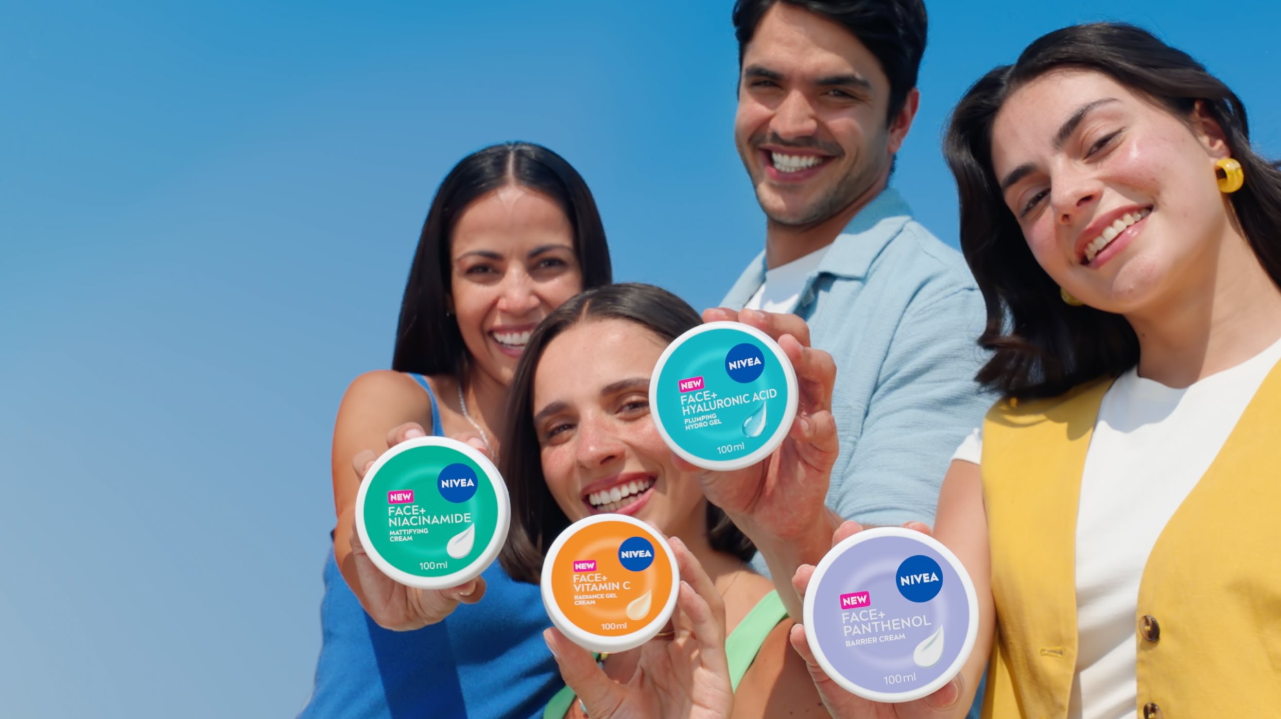 Lächelnde Menschen präsentieren NIVEA FACE+ Creme-Tiegel in Türkis, Orange, Blau und Violett. Jeder Tiegel trägt das NIVEA FACE+ Logo und unterscheidet sich durch seine charakteristische Farbgebung.