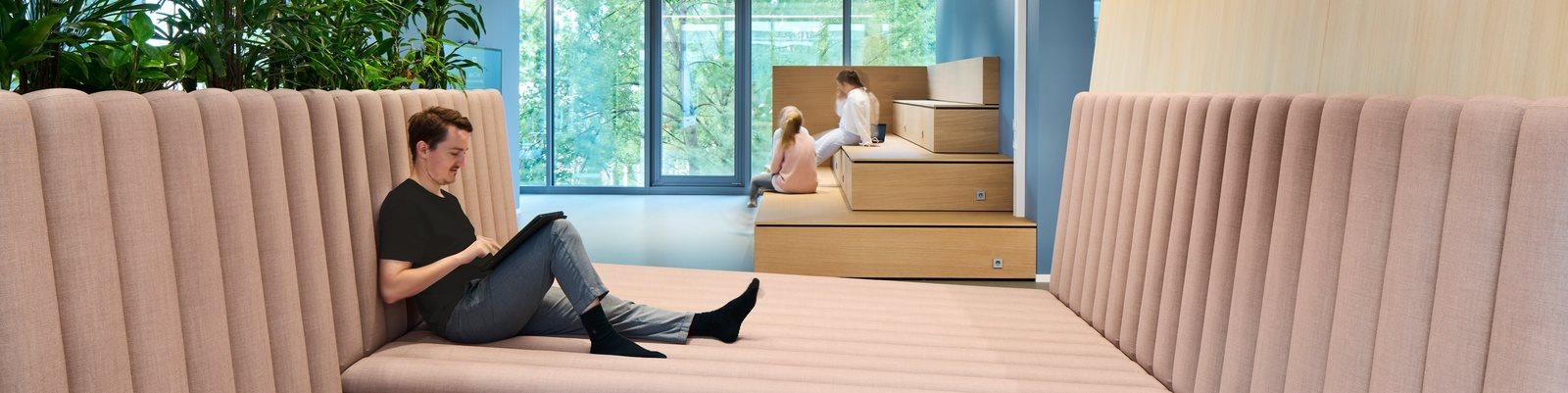 A high-angle 3D architectural rendering of a modern office complex or corporate campus composed of several interconnected white, rectangular buildings. The structures are arranged in a U-shape around central courtyards and are surrounded by green space with manicured trees and walking paths. Translucent blue text labels, including "tesa," "Eucerin," and "La Prairie," are superimposed over different sections of the buildings, indicating specific brand areas within the campus.