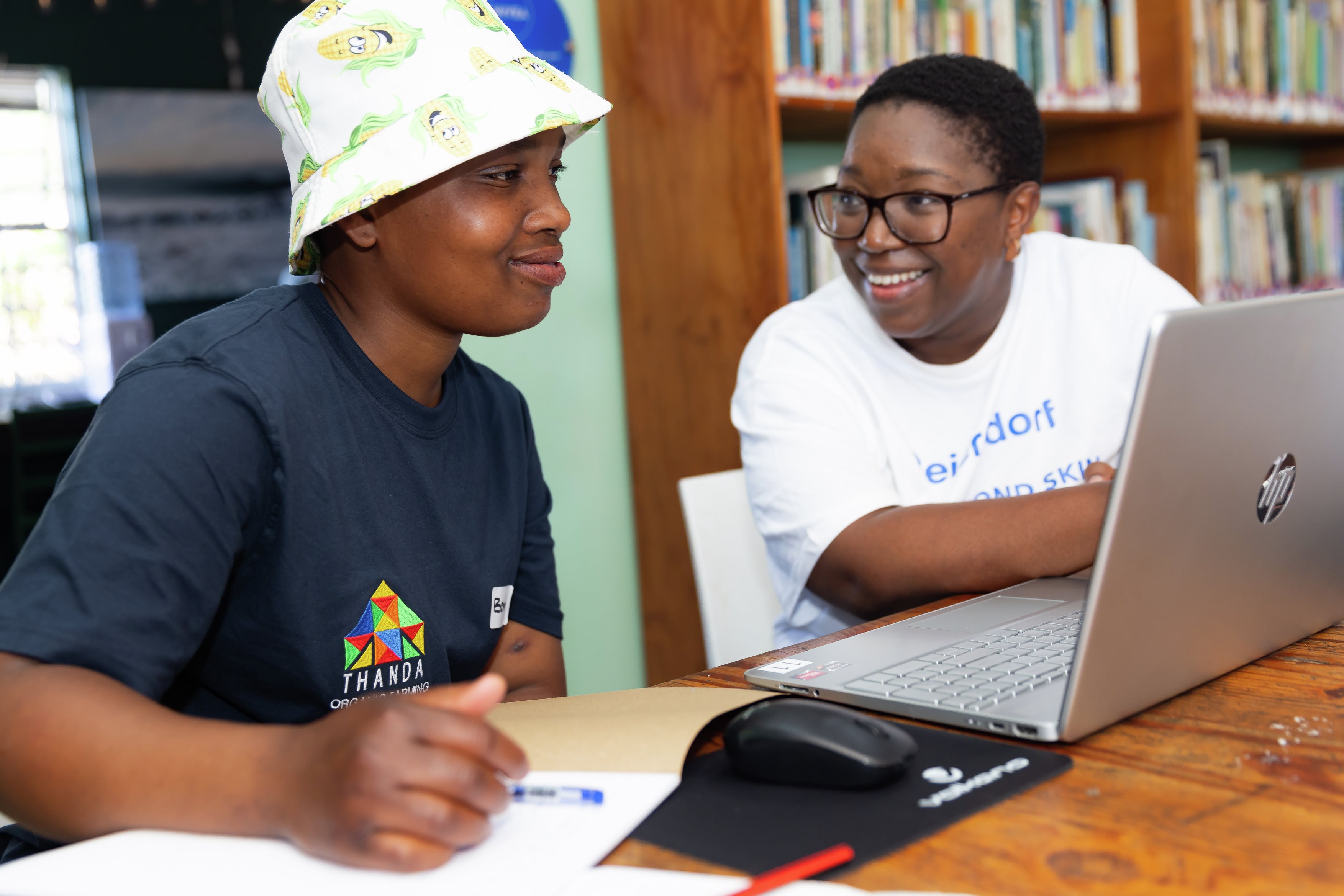 Two women sitting in front of a laptop and smiling together at CARE BEYOND SKIN Day