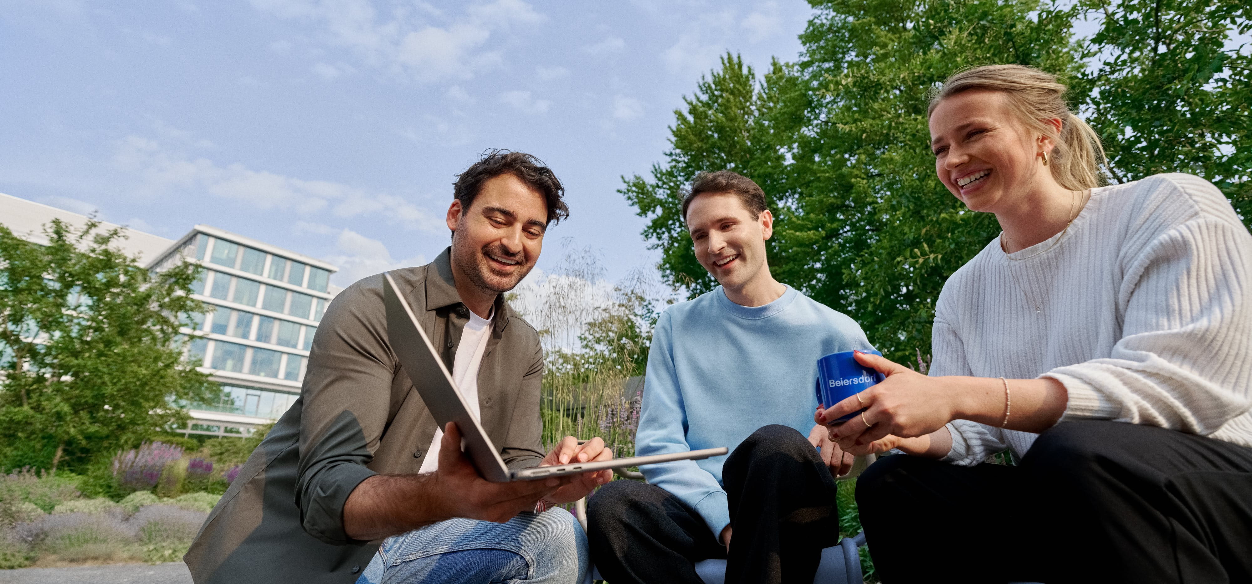 Beiersdorf Mitarbeitende arbeiten im Außenbereich gemeinsam an einem Projekt und stehen für Teamarbeit, Flexibilität und ein modernes Arbeitsumfeld.