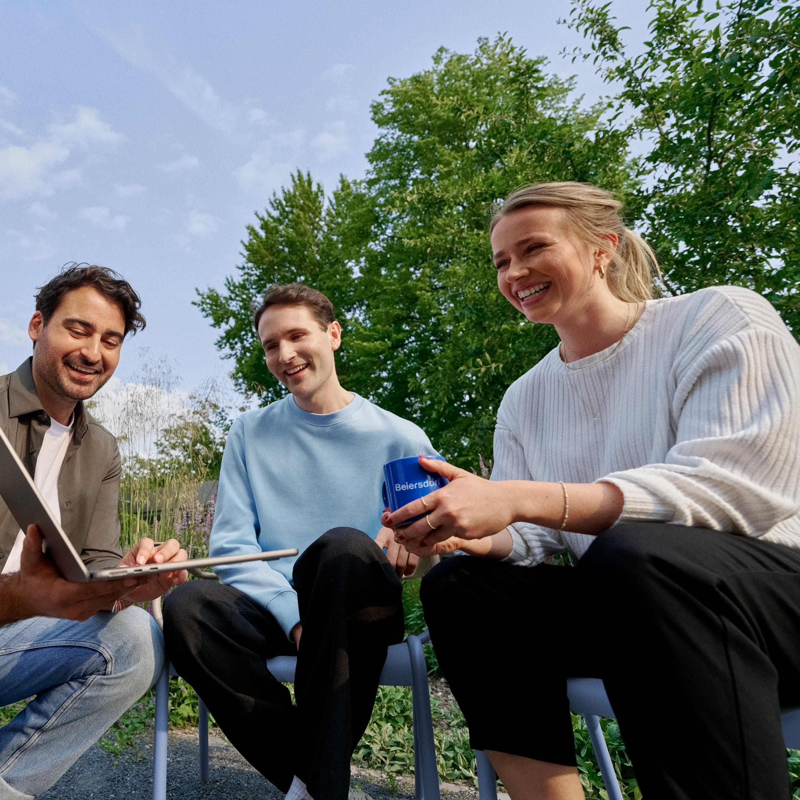 Beiersdorf Mitarbeitende arbeiten im Außenbereich gemeinsam an einem Projekt und stehen für Teamarbeit, Flexibilität und ein modernes Arbeitsumfeld.