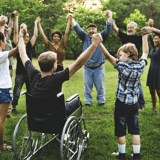 Diverse group of people holding hands in a circle outdoors, representing inclusion and togetherness.