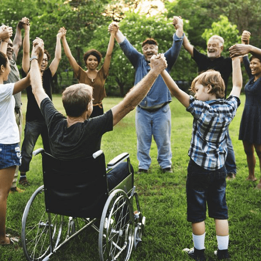 Diverse group of people holding hands in a circle outdoors, representing inclusion and togetherness.