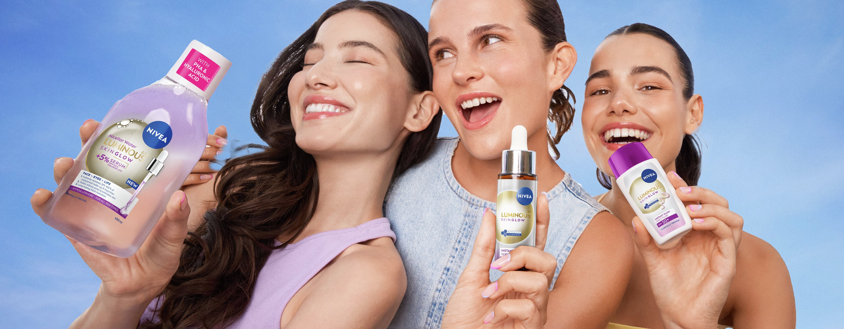 Group of friends smiling closely together outdoors, with one person holding up a NIVEA skincare product bottle, conveying joy, confidence, and shared moments.
