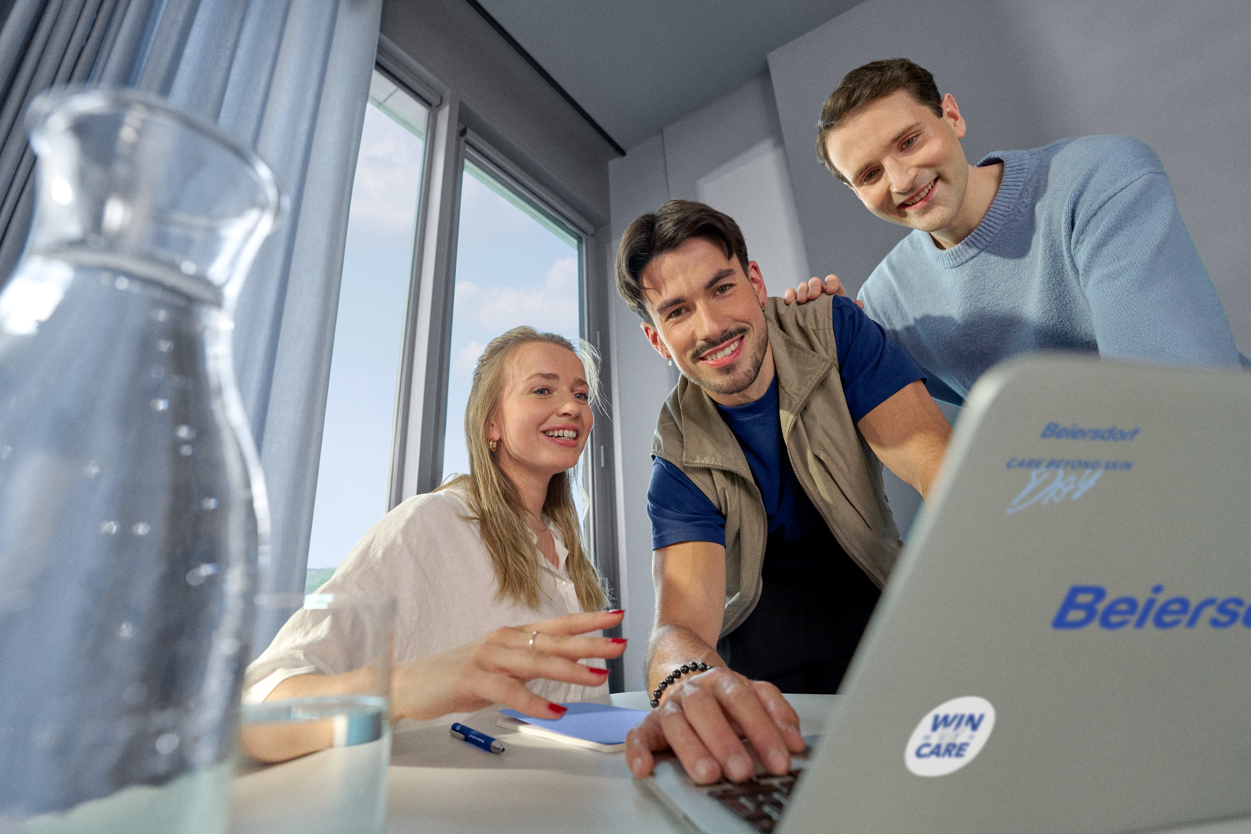 Beiersdorf Mitarbeitende besprechen Projektinhalte an einem Laptop und stehen für Zusammenarbeit, Innovation und Karrieremöglichkeiten in einem globalen Team.